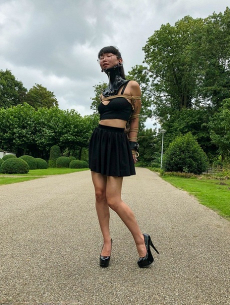 Asian chick Flawless Meow wears a neck collar with her arms bound in a park 29819748